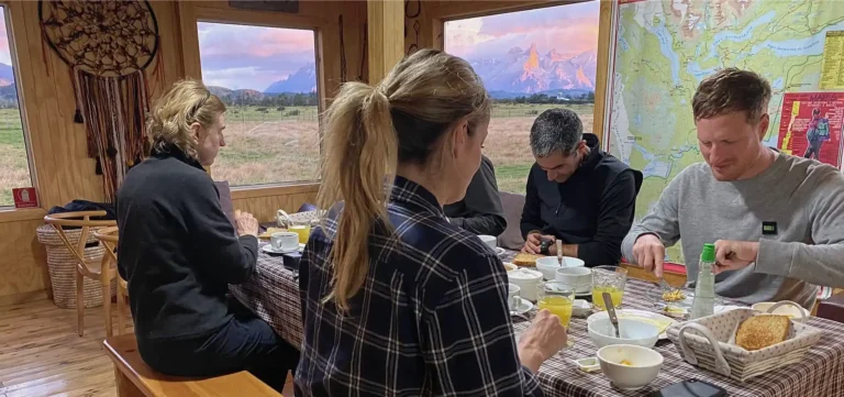 Café y desayuno servido en una mesa junto al ventanal del refugio Vista al Paine durante las luces doradas del amanecer en la Patagonia.