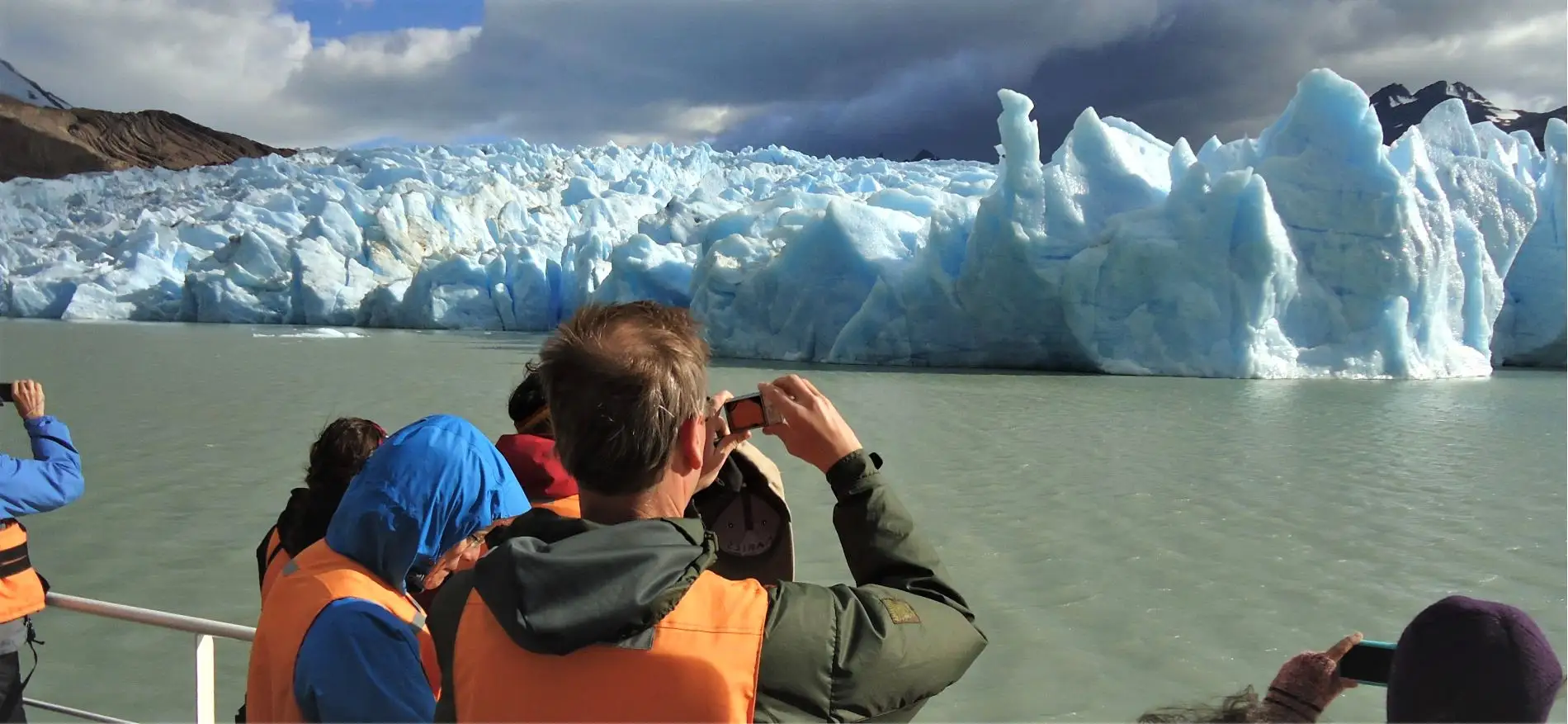 Pasajeros tomando fotografías desde la cubierta de un barco frente a la imponente pared de hielo azul del Glaciar Grey.
