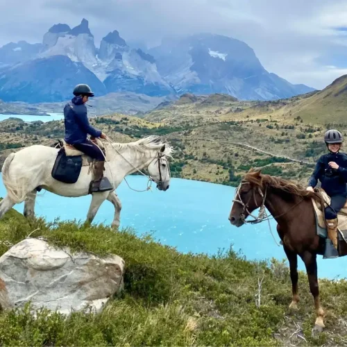 Group of riders on a guided horseback tour next to the Paine River with a direct view of the Cuernos del Paine viewpoint in Patagonia.
