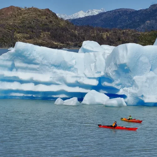 Adventurers paddling in double and single kayaks near massive ice blocks calved from the Grey Glacier.