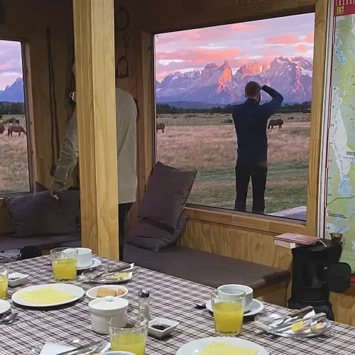 Coffee and breakfast served on a table by the window at Vista al Paine refuge during the golden light of a Patagonian sunrise.